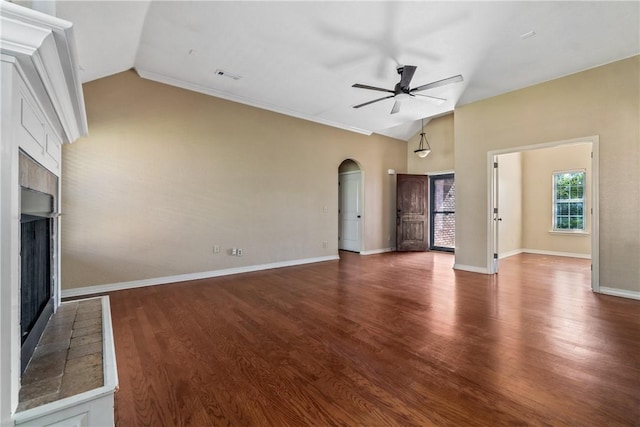 unfurnished living room featuring a fireplace with raised hearth, vaulted ceiling, a ceiling fan, arched walkways, and wood finished floors