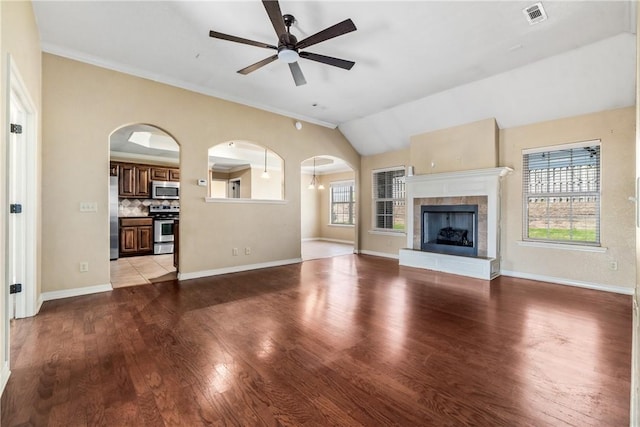 unfurnished living room with ceiling fan, arched walkways, wood finished floors, baseboards, and vaulted ceiling