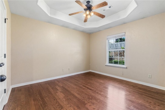 unfurnished room featuring a tray ceiling, wood finished floors, ceiling fan, and baseboards