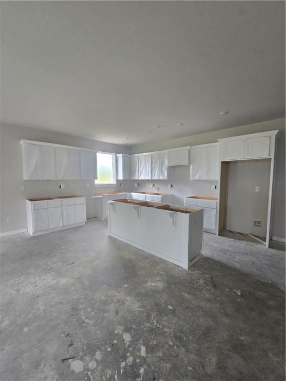 2308 Lexington St, Siloam Springs, AR 72761 - kitchen featuring a center island, concrete flooring, white cabinetry, and a kitchen bar