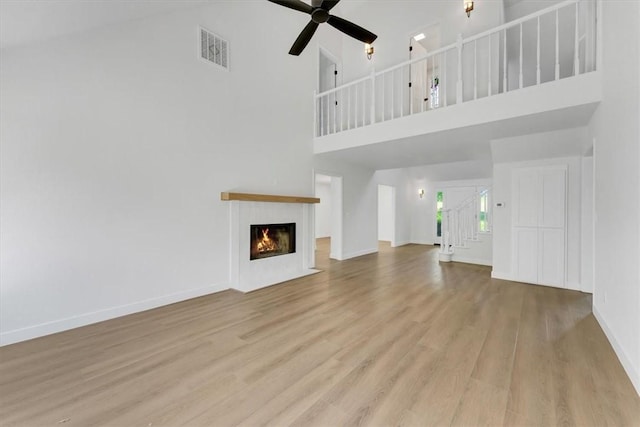 12391 Shamrock Rd, Farmington, AR 72730 - unfurnished living room with a towering ceiling, wood finished floors, a ceiling fan, baseboards, and a lit fireplace