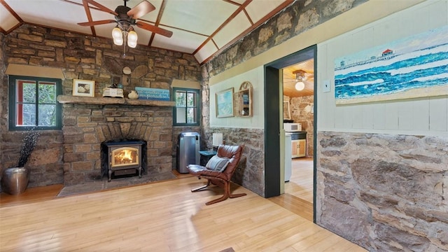 living area with ceiling fan, wood finished floors, a wood stove, and lofted ceiling