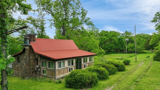 rear view of house with stone siding, metal roof, a chimney, a forest view, and a yard