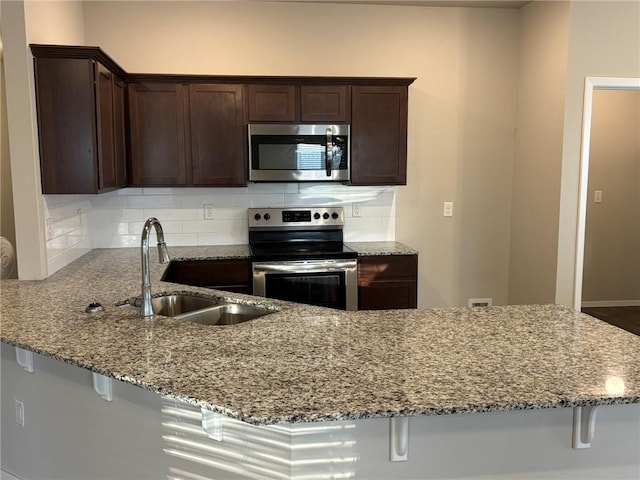 811 Belhaven Rd, Centerton, AR 72719 - kitchen featuring appliances with stainless steel finishes, a sink, tasteful backsplash, light stone countertops, and dark brown cabinets