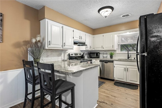 1801 Jean St, Springdale, AR 72762 - kitchen with black appliances, a peninsula, under cabinet range hood, light stone countertops, and white cabinets