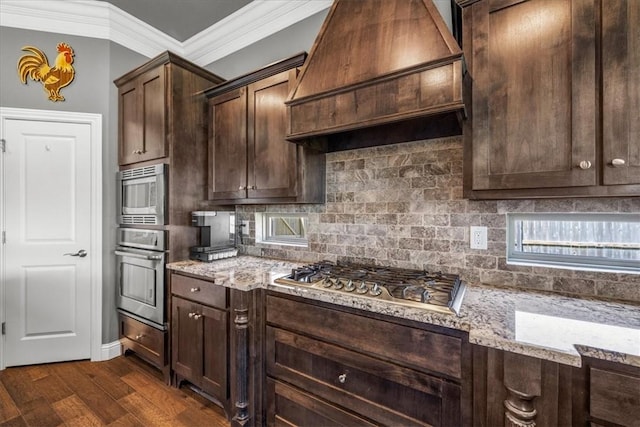 kitchen with custom range hood, appliances with stainless steel finishes, crown molding, light stone counters, and decorative backsplash