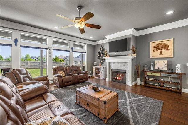 living room with crown molding, ceiling fan, plenty of natural light, a lit fireplace, and baseboards