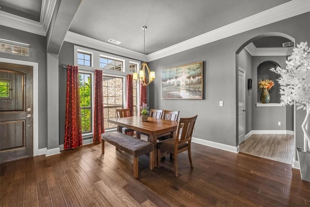 dining area featuring dark wood-style floors, a chandelier, baseboards, crown molding, and arched walkways