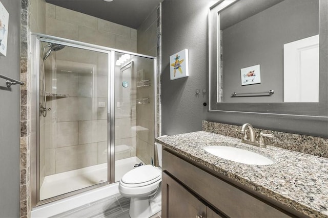 full bath featuring toilet, a stall shower, vanity, and a textured wall