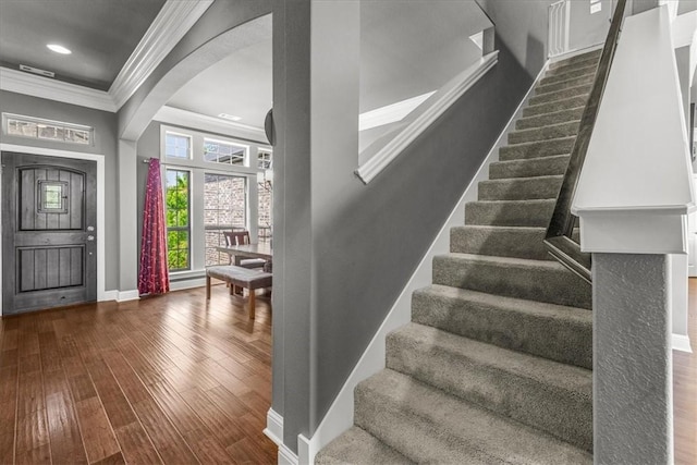entrance foyer featuring crown molding, arched walkways, dark wood-type flooring, stairs, and baseboards