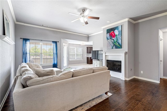 living area featuring a ceiling fan, baseboards, ornamental molding, dark wood-style flooring, and a fireplace