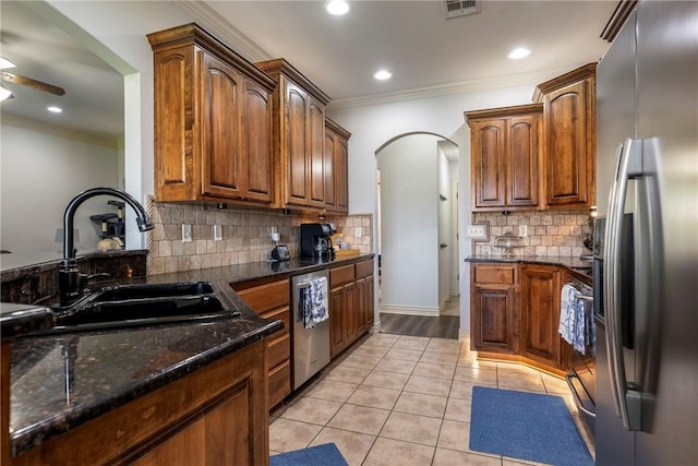 kitchen featuring appliances with stainless steel finishes, a sink, ornamental molding, arched walkways, and tasteful backsplash