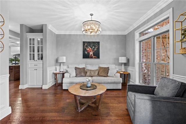 living area featuring a chandelier, dark wood-style flooring, a wainscoted wall, and crown molding