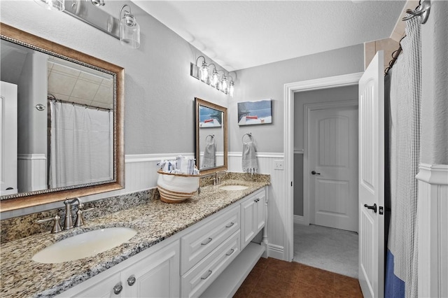 full bathroom with a wainscoted wall, double vanity, and tile patterned flooring