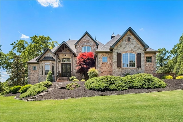 french provincial home featuring a front yard, french doors, brick siding, and stone siding