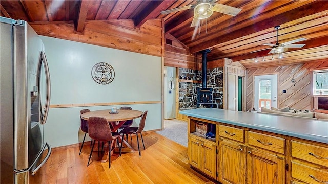 kitchen featuring freestanding refrigerator, a wood stove, a ceiling fan, light wood-style floors, and wooden ceiling