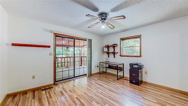 office space with light wood-type flooring, ceiling fan, baseboards, and a textured ceiling