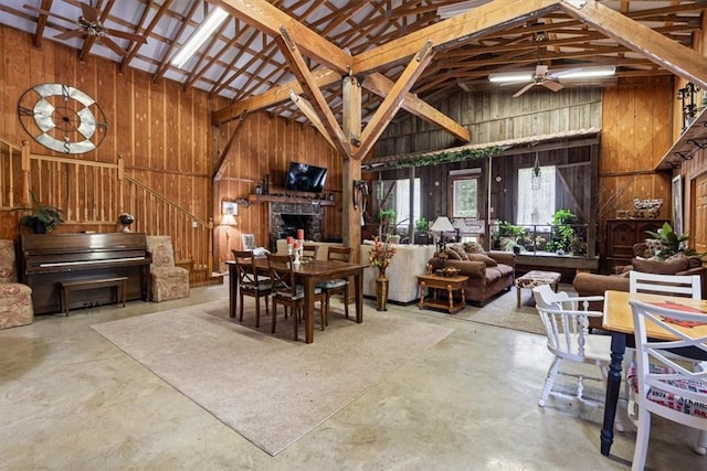dining room featuring high vaulted ceiling, ceiling fan, wooden walls, finished concrete flooring, and stairway