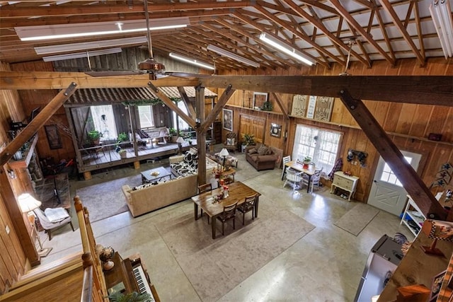 living room featuring vaulted ceiling, wooden walls, concrete flooring, and ceiling fan
