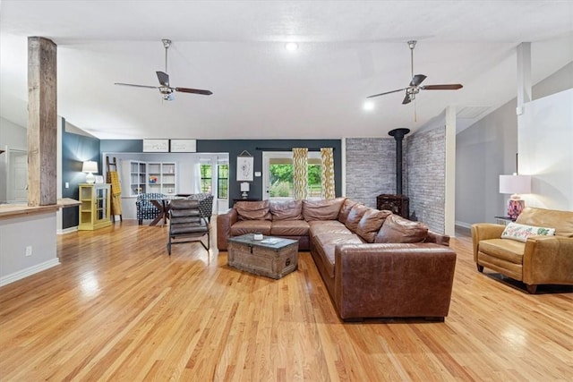 living room featuring ceiling fan, vaulted ceiling, a wood stove, light wood finished floors, and baseboards