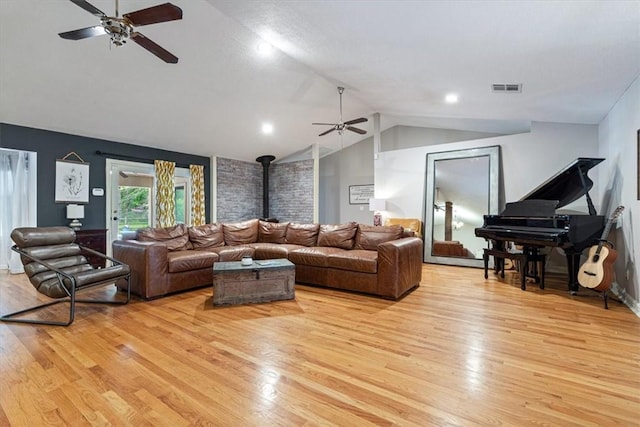 living room featuring ceiling fan, light wood finished floors, lofted ceiling, and a wood stove