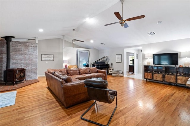 living area with ceiling fan, lofted ceiling, wood finished floors, and a wood stove