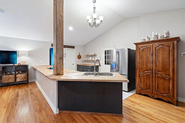 kitchen featuring a sink, stainless steel fridge, lofted ceiling, a peninsula, and light wood-style floors