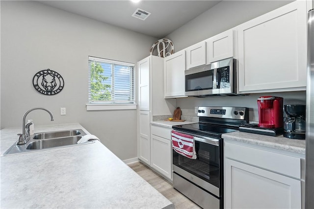 293 W Ash St Unit 1, Fayetteville, AR 72703 - kitchen with stainless steel appliances, a sink, light countertops, white cabinetry, and light wood-style floors