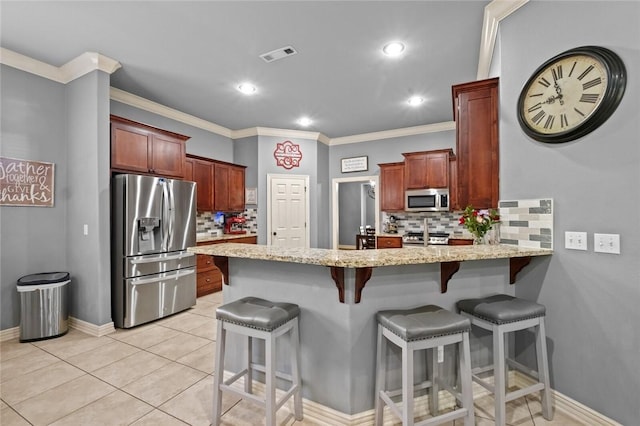 kitchen featuring appliances with stainless steel finishes, a peninsula, decorative backsplash, light stone countertops, and a kitchen bar