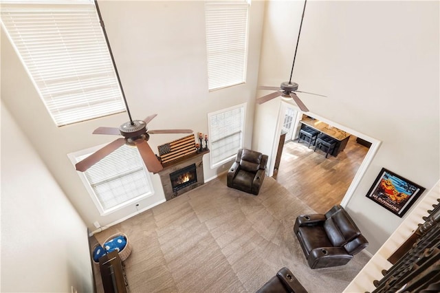 unfurnished living room with ceiling fan, a high ceiling, a lit fireplace, and carpet floors