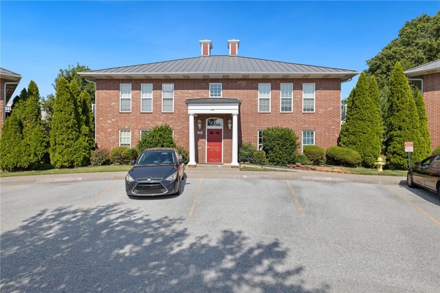 413 Columbia Pl, Lowell, AR 72745 - view of front of house featuring a standing seam roof, uncovered parking, brick siding, a chimney, and metal roof