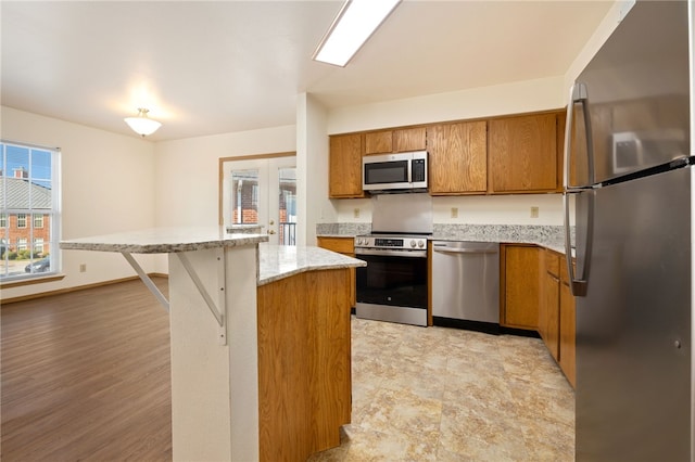 413 Columbia Pl, Lowell, AR 72745 - kitchen featuring stainless steel appliances, brown cabinetry, a kitchen island, light stone counters, and a breakfast bar area