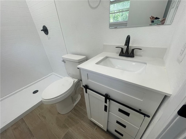 401 Walnut St, Clarksville, AR 72830 - full bathroom with toilet, vanity, a tile shower, wood finished floors, and a textured wall