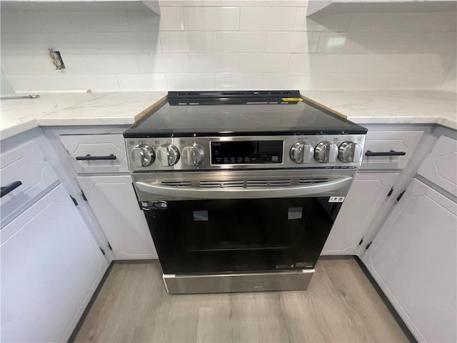 401 Walnut St, Clarksville, AR 72830 - kitchen featuring stainless steel range with electric cooktop, light wood finished floors, white cabinetry, and decorative backsplash