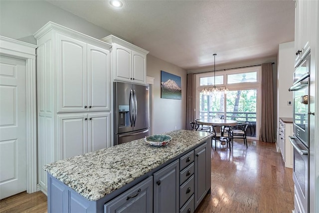 2507 NW Linebarger Ln, Bentonville, AR 72712 - kitchen featuring appliances with stainless steel finishes, white cabinets, wood finished floors, light stone countertops, and a center island