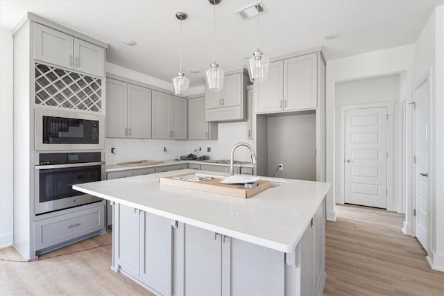 6601 SW Acacia St, Bentonville, AR 72713 - kitchen with stainless steel oven, gray cabinets, built in microwave, light wood finished floors, and a center island with sink