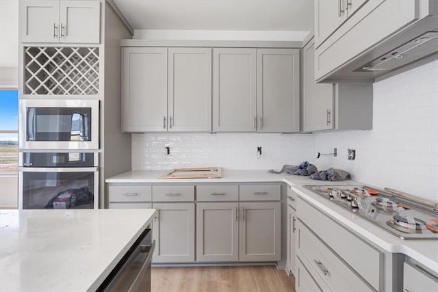 6601 SW Acacia St, Bentonville, AR 72713 - kitchen with stainless steel appliances, gray cabinetry, light wood-type flooring, and under cabinet range hood