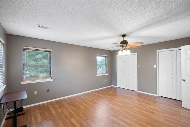 1433 Shalimar Cir, Russellville, AR 72802 - unfurnished bedroom with light wood finished floors, two closets, a textured ceiling, baseboards, and a ceiling fan