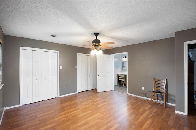 1433 Shalimar Cir, Russellville, AR 72802 - unfurnished bedroom featuring wood finished floors, multiple closets, baseboards, a textured ceiling, and a ceiling fan