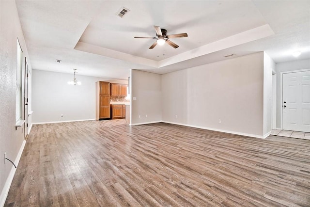 515 Jenkins Rd, Prairie Grove, AR 72753 - unfurnished living room featuring a raised ceiling, light wood-style floors, ceiling fan, baseboards, and a chandelier