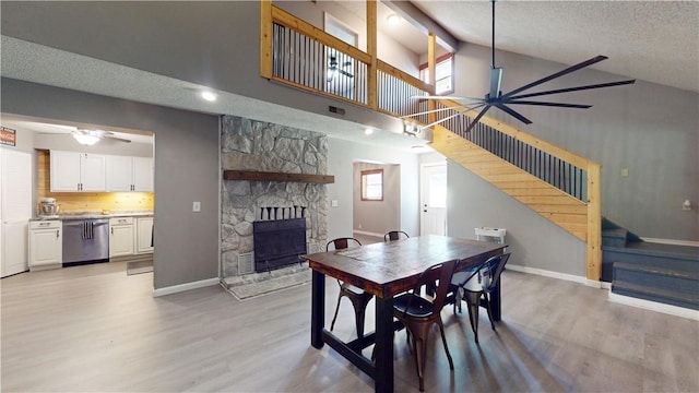 104 NE Deer Ridge Rd, Gravette, AR 72736 - dining space featuring ceiling fan, stairs, high vaulted ceiling, a fireplace, and light wood-type flooring