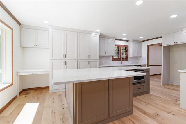 1640 N Boston Pl, Fayetteville, AR 72703 - kitchen featuring tasteful backsplash, light countertops, light wood finished floors, a center island, and white cabinets