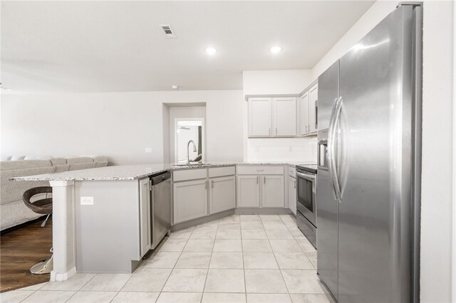 2405 Maplewood Ave, Lowell, AR 72745 - kitchen featuring stainless steel appliances, a peninsula, open floor plan, light stone counters, and light tile patterned floors