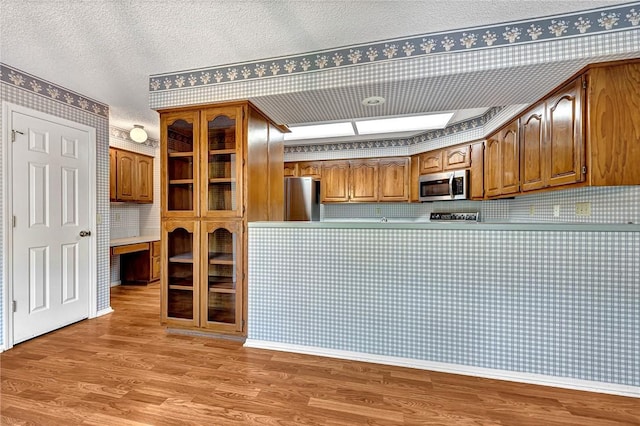 22 Marina Cir, Bella Vista, AR 72715 - kitchen with appliances with stainless steel finishes, wood finished floors, wallpapered walls, brown cabinetry, and a textured ceiling