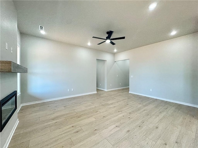 6002 SW Desert Ave, Bentonville, AR 72713 - unfurnished living room with a ceiling fan, a glass covered fireplace, light wood finished floors, recessed lighting, and a textured ceiling