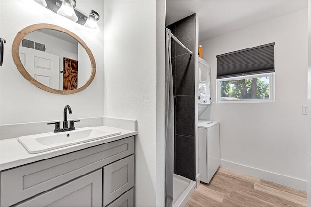 312 NW J St, Bentonville, AR 72712 - bathroom with estacked washer and dryer, vanity, a stall shower, and wood finished floors