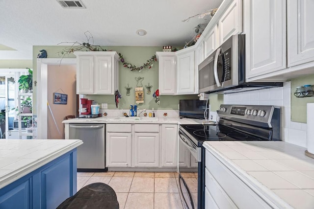 2977 Quartz Dr, Fayetteville, AR 72704 - kitchen featuring appliances with stainless steel finishes, a sink, white cabinets, tile countertops, and light tile patterned flooring