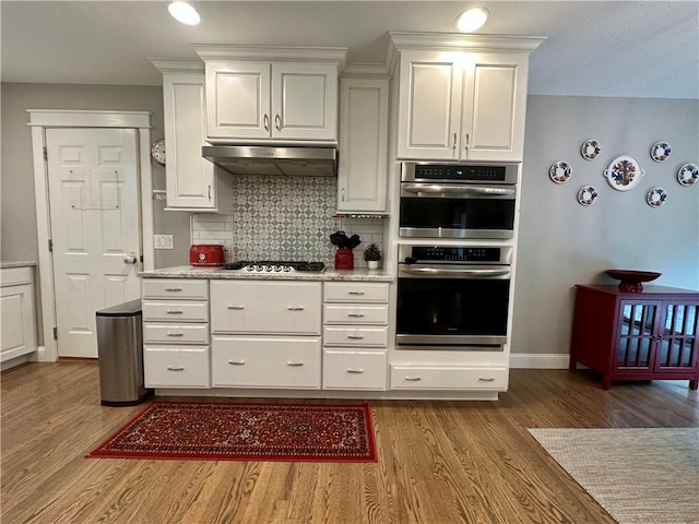 9193 Grimes Dr, Rogers, AR 72756 - kitchen with under cabinet range hood, wood finished floors, stainless steel appliances, white cabinetry, and backsplash