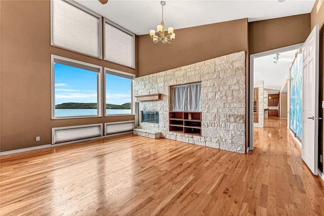 289 County Road 1521, Eureka Springs, AR 72632 - unfurnished living room featuring a chandelier, a stone fireplace, wood finished floors, a towering ceiling, and a water view