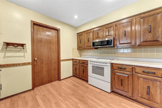 2001 W Magnolia St, Rogers, AR 72758 - kitchen with stainless steel microwave, white electric stove, light wood-style flooring, brown cabinetry, and a textured ceiling